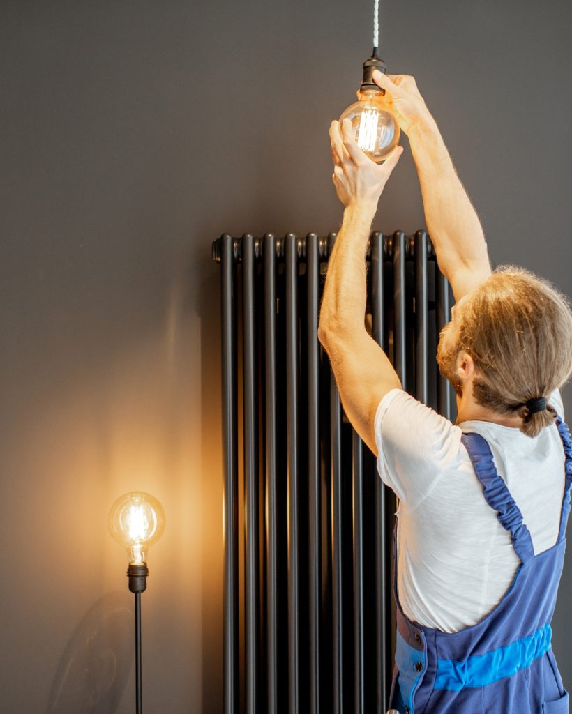 Handyman in uniform replacing lightbulb in the living room at home